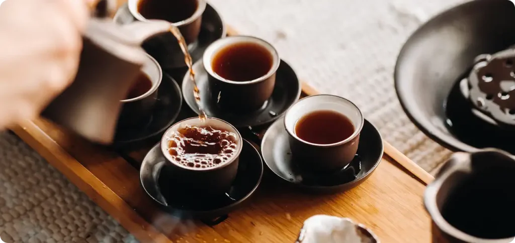 Ceremonia parzenia herbaty na bambusowym stole, jeden z uczestników nalewa herbatę.